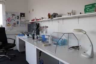 Helles Labor mit langen Arbeitstischen, Werkzeugen und Materialien für Elektronikreparaturen.