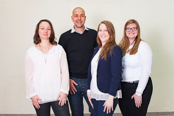 Vier lächelnde Kollegen stehen im Büro und präsentieren Teamarbeit und Zusammenarbeit.